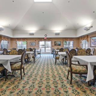 A well-lit dining room with multiple tables and chairs arranged neatly on a patterned carpet.
