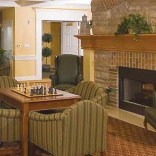 A cozy living room featuring a chessboard on a wooden table, surrounded by striped armchairs and a warm fireplace.