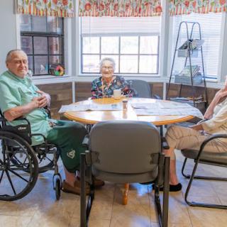 A group of elderly individuals engaging in conversation around a table in a care facility.