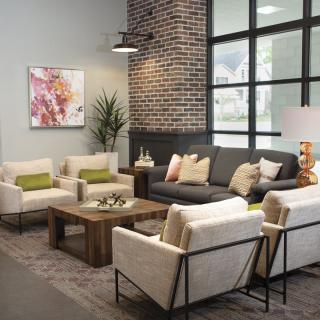 A modern living room with a gray sofa, cream chairs, and a wooden coffee table, complemented by a brick accent wall and decorative plants.