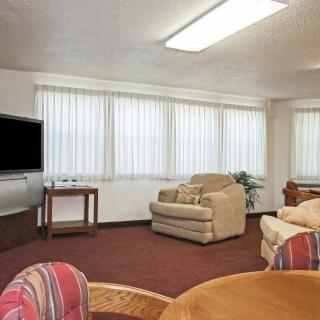 A cozy living room with armchairs, a television, and large windows with blinds.