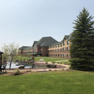 A large brick building with a well-maintained garden and trees in the foreground.