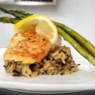 A plate featuring a grilled chicken breast on a bed of rice, garnished with asparagus and a lemon slice.