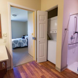 A view of a bathroom with an adjacent laundry area leading into a bedroom.