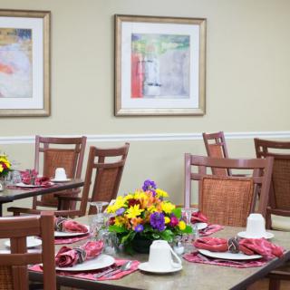 A well-arranged dining room with tables set for a meal, featuring colorful flowers and framed artwork on the walls.