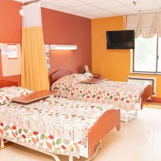 A brightly colored hospital patient room equipped with two beds and a television.