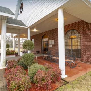 A welcoming building entrance with a covered porch, white columns, and landscaped greenery.