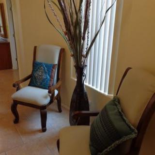 A cozy seating area with two upholstered chairs, decorative pillows, and a tall vase with branches.