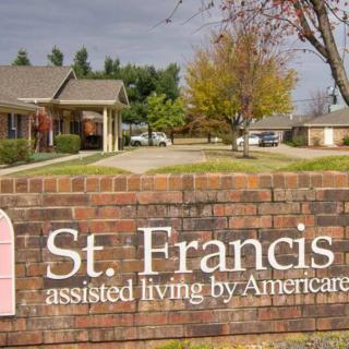 A brick wall sign for St. Francis assisted living by Americare, with a building and trees in the background.