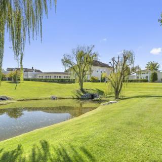 A serene golf course landscape featuring a pond, lush grass, trees, and a modern building under a clear blue sky.