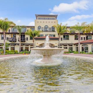 A luxurious building with a large fountain in the foreground, surrounded by palm trees on a sunny day.