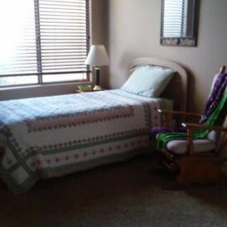 A cozy bedroom with a single bed, patterned quilt, and a rocking chair by the window.