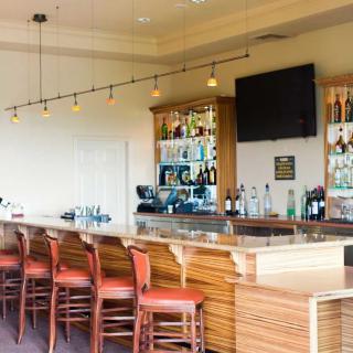 A modern bar with a sleek counter and empty red chairs, featuring a liquor display and a television on the wall.