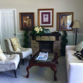 A cozy living room with elegant furniture and decor, featuring a sofa, chairs, coffee table, artwork on the walls, and decorative plants.