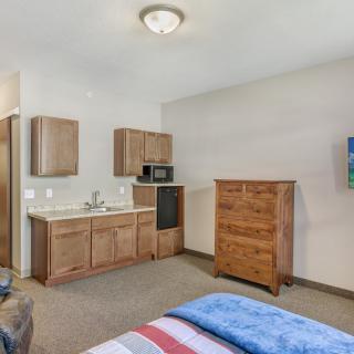 A cozy bedroom with a kitchenette, featuring a microwave and a wooden dresser.