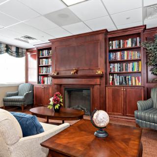 A cozy library room with bookshelves, a fireplace, and comfortable seating arrangements.