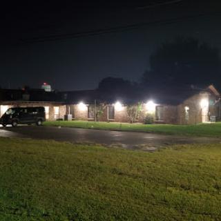 A well-lit house at night with a parked vehicle and lush green grass.