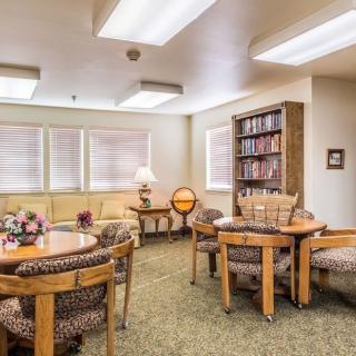 A cozy living room with tables, chairs, bookshelves, and soft lighting.