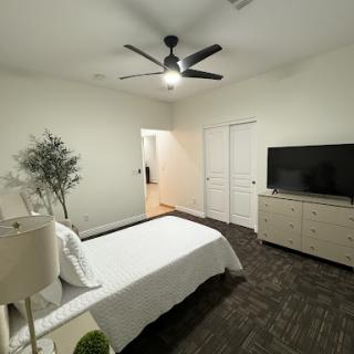 A serene and modern bedroom featuring minimalistic decor, a ceiling fan, and a television.