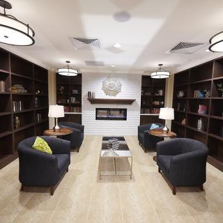 A modern library seating area with armchairs, bookshelves, and a central fireplace.