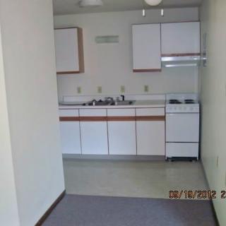 A small apartment kitchen with white cabinets, a stove, and a sink.