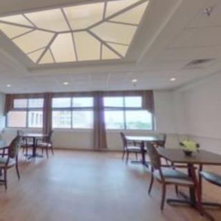 A spacious dining area with several tables and chairs, featuring large windows and an elegant ceiling design.
