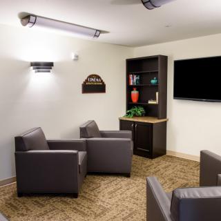 A modern lounge area featuring comfortable chairs, a television, and a bookshelf.