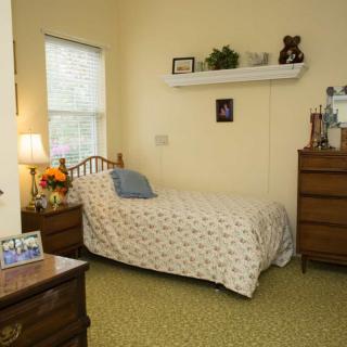 A cozy bedroom with a single bed, dresser, and decorative shelf.