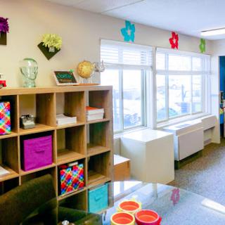 A bright and colorful office space featuring organized shelves and large windows allowing natural light.