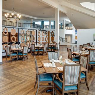 A spacious and elegantly designed restaurant interior featuring neatly arranged tables and chairs, with decorative elements and chandeliers.
