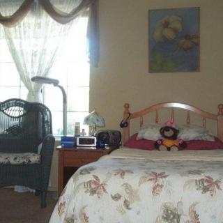 A cozy bedroom with a neatly made bed, a bedside table with a lamp, and a chair by the window.