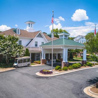 A building entrance with landscaped surroundings and a vehicle parked nearby under a blue sky.