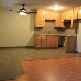 An empty apartment kitchen and living area with wood cabinets and a ceiling fan.