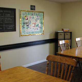 A cozy dining area featuring wooden tables and chairs, adorned with a piece of framed art and a chalkboard.