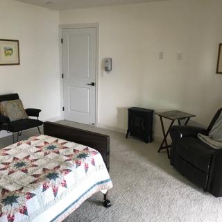 A minimalist bedroom with a quilt-covered bed, chairs, and small tables.