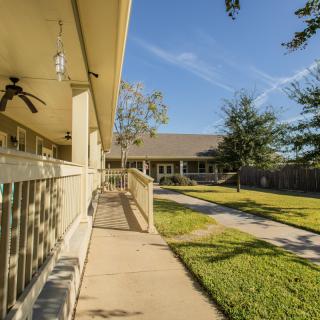 A sunny view of a house with a large yard, pathway, and porch.