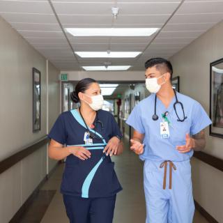 Two healthcare professionals in conversation while walking down a hospital hallway.