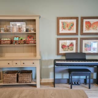 A cozy room with a small piano and a wooden cabinet displaying decorative items, complemented by four framed butterfly artworks on the wall.