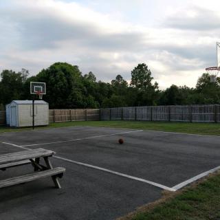 An outdoor basketball court with a bench and a basketball hoop under a cloudy sky.