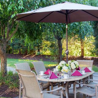 A beautifully set outdoor patio table under an umbrella, surrounded by lush greenery.