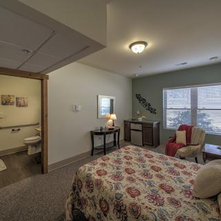 A cozy bedroom with a bed, armchair, and lamp near a window.