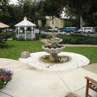 A scenic garden with a central fountain and a white gazebo surrounded by lush greenery.