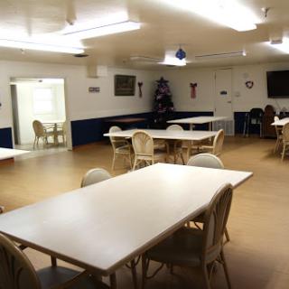A spacious community room featuring several tables and chairs, ready for activities.