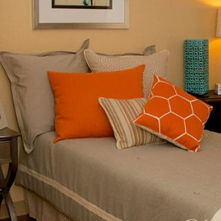 A cozy bedroom setup with neutral-toned bedding and vibrant orange accent pillows.
