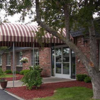 A view of a building entrance with a striped awning, brick exterior, and surrounding landscaping.