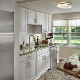 A modern kitchen with white cabinets, stainless steel appliances, and granite countertops, illuminated by natural light from large windows.