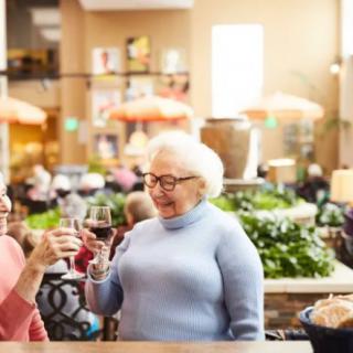 Two elderly women enjoying wine and conversation in a lively restaurant setting.