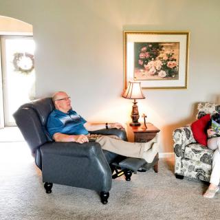 Two people relaxing in a comfortable living room setting, one seated in a recliner and the other on an armchair.