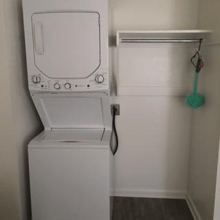 A compact laundry space with stacked washer and dryer units and an adjacent shelf.
