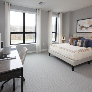 A modern bedroom with large windows, a comfortable bed, and a work desk.